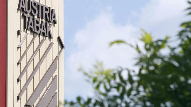 Das Logo von Austria Tabak an einer Fassade vor blauem Himmel und Bäumen.