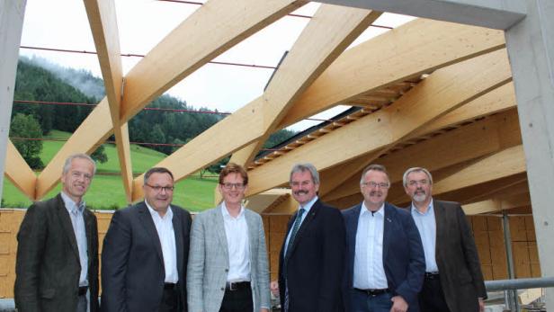 Eine Gruppe von sechs Männern steht vor einer Holzkonstruktion im Bau.