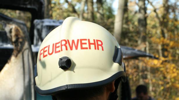Ein Feuerwehrhelm vor einem ausgebrannten Fahrzeug.