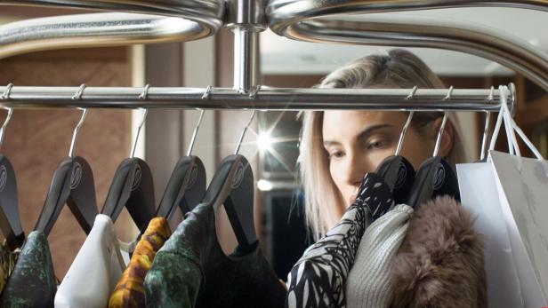 Eine Frau betrachtet Kleidung auf einer Kleiderstange und Einkaufstaschen.