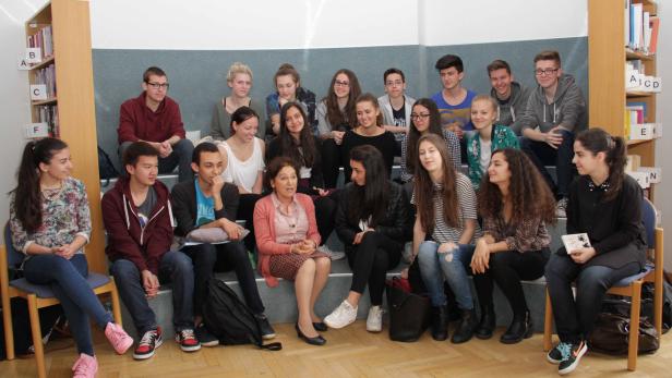 Eine Gruppe von Schülern sitzt mit einer Lehrerin in einem Raum mit Bücherregalen.