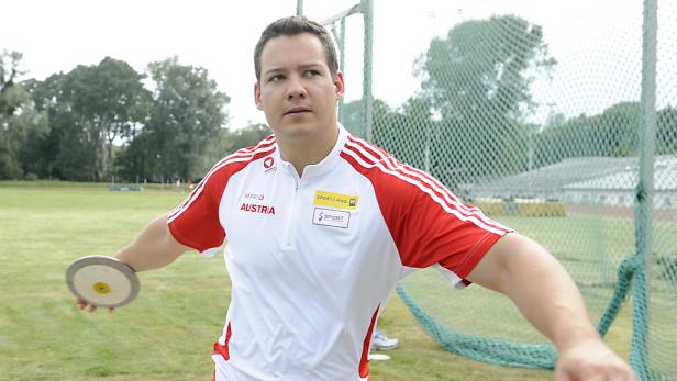 Ein Diskuswerfer in österreichischer Sportbekleidung bereitet sich auf einen Wurf vor.