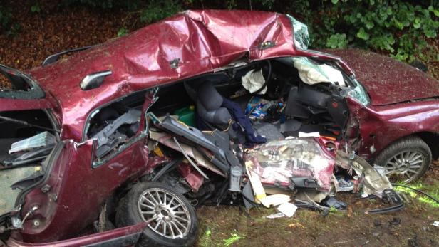 Ein stark beschädigtes, rotes Auto nach einem Unfall.