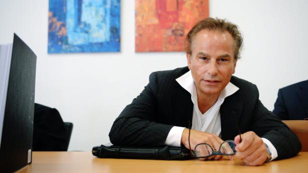 Ein Mann in Anzug sitzt an einem Tisch mit Brille in der Hand.