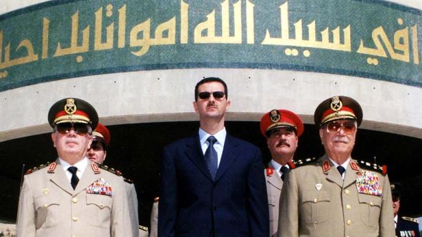Baschar al-Assad mit Militärangehörigen vor einem Gebäude mit arabischer Schrift.