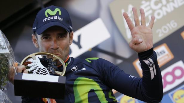 Ein Radrennfahrer küsst seine Trophäe und zeigt mit der Hand die Zahl Vier.