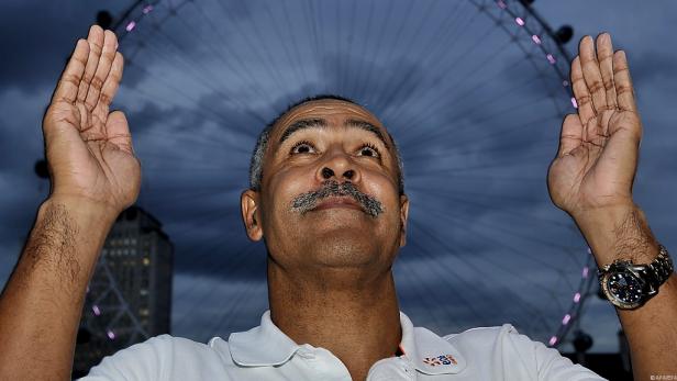 Ein Mann mit erhobenen Händen vor dem London Eye.