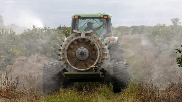Ein Traktor sprüht Pestizide auf einem Feld mit Obstbäumen.