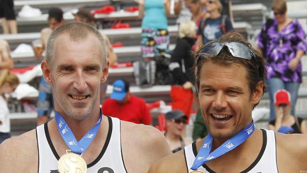 Zwei Beachvolleyballspieler mit Medaillen lächeln in die Kamera.