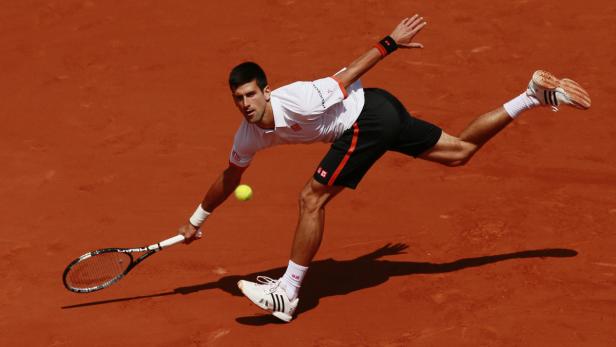 Novak Đoković schlägt einen Tennisball auf einem Sandplatz.