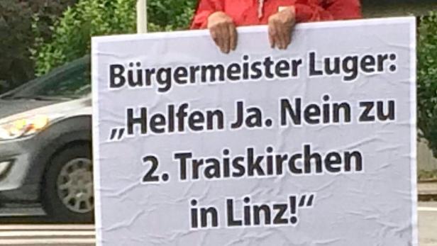 Eine Person hält ein Schild mit der Aufschrift: „Bürgermeister Luger: Helfen Ja. Nein zu 2. Traiskirchen in Linz!“.