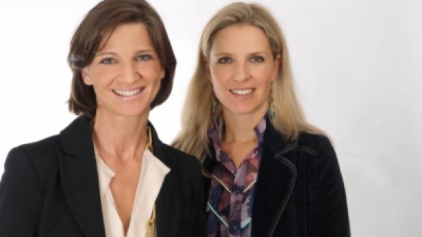 Zwei Frauen lächeln in die Kamera, beide tragen Blazer.