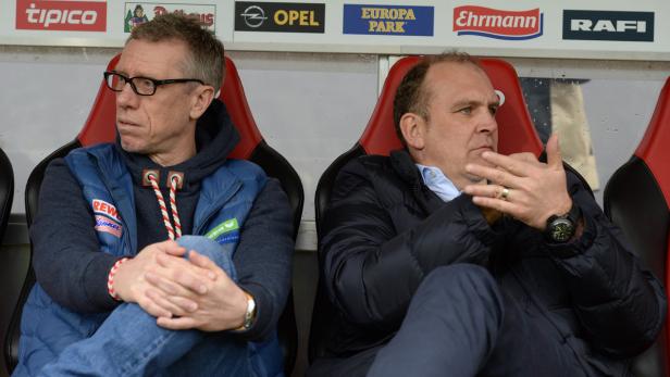 Zwei Männer sitzen auf einer Bank vor Werbetafeln.