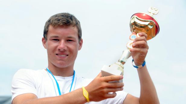 Ein junger Mann hält lächelnd eine Trophäe in die Höhe.