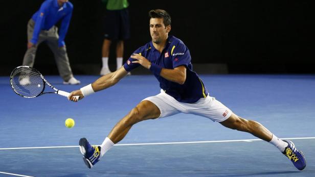 Novak Đoković schlägt einen Tennisball auf einem blauen Platz.