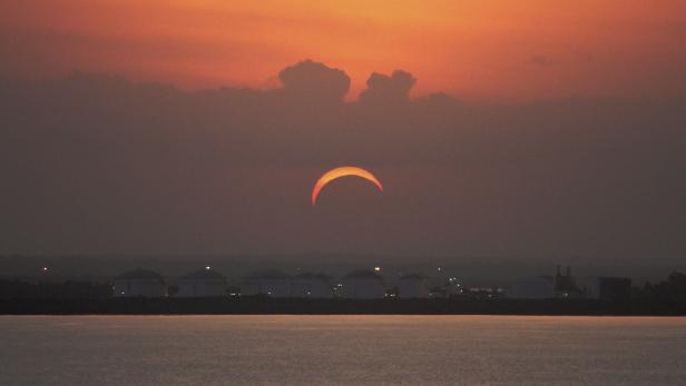 Eine ringförmige Sonnenfinsternis über dem Wasser bei Sonnenuntergang.