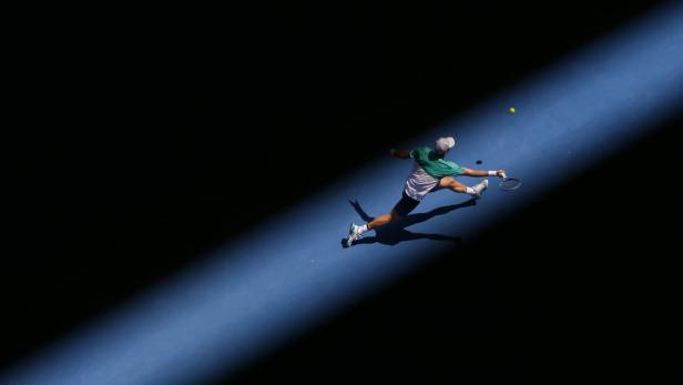 Ein Tennisspieler schlägt den Ball auf einem blauen Platz.