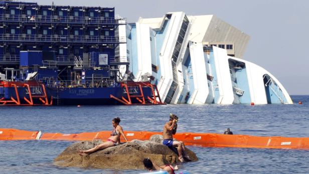 Die Costa Concordia liegt vor der Insel Giglio im Wasser, während sich Badegäste am Strand aufhalten.