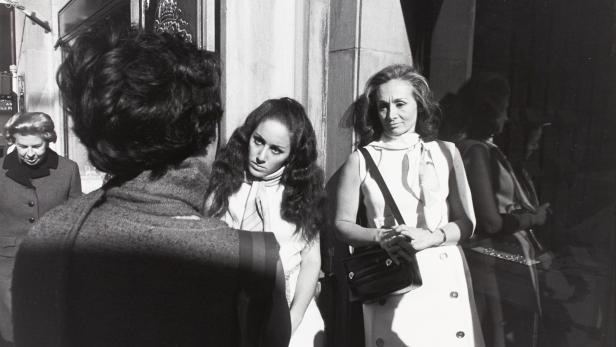 Drei Frauen stehen vor einem Gebäude in einer Schwarzweißaufnahme.