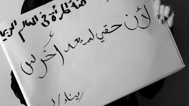 Eine Frau mit verklebtem Mund hält ein Schild mit arabischer Schrift hoch.