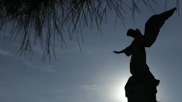 Die Silhouette einer Engelsstatue vor einem hellen Himmel.