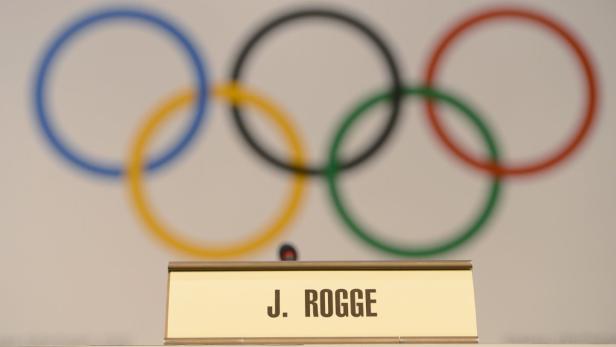 Das Logo der Olympischen Spiele hinter einem Namensschild mit der Aufschrift „J. Rogge“.
