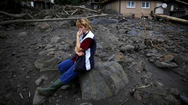 Eine Frau sitzt auf einem Felsen inmitten von Schlamm und Trümmern und weint.