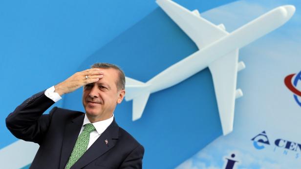 Recep Tayyip Erdoğan salutiert vor einem Modellflugzeug.