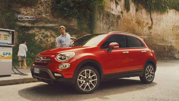Ein roter Fiat 500X steht an einer Tankstelle, während ein Mann daneben steht.