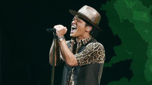 Bruno Mars singt mit Hut und Leopardenmusterhemd auf der Bühne.