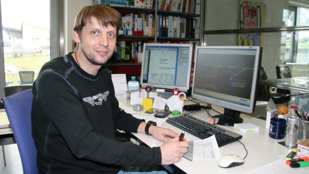 Ein Mann sitzt an einem Schreibtisch mit zwei Computermonitoren und arbeitet an einem Dokument.