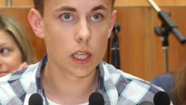 Ein junger Mann spricht bei einer Veranstaltung in mehrere Mikrofone.