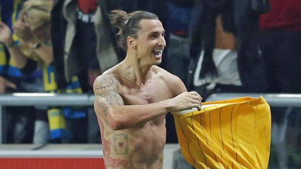 Ein lächelnder, barfüßiger Zlatan Ibrahimović hält ein gelbes Trikot in der Hand.