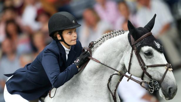 Eine Reiterin mit Helm auf einem Schimmelpferd bei einem Reitturnier.