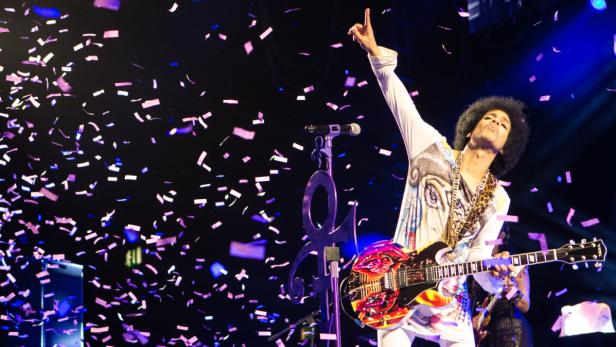 Prince spielt Gitarre auf der Bühne, während Konfetti in der Luft schwebt.
