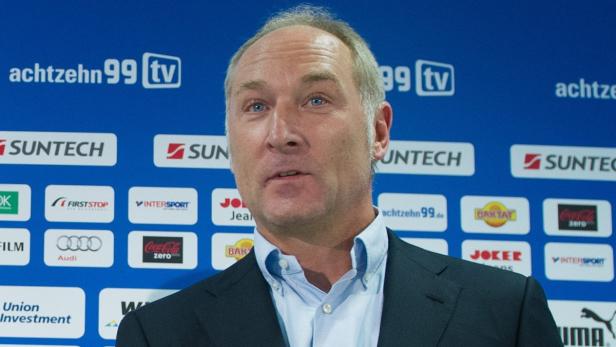 Ein Mann in Anzug steht vor einer Wand mit Sponsorenlogos.