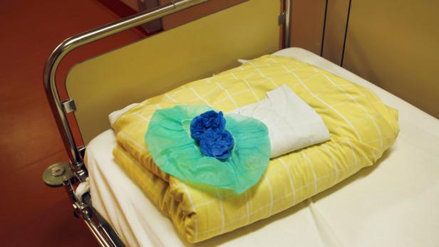 Ein Krankenhausbett mit gelber Bettwäsche, einer Haube und Handschuhen.