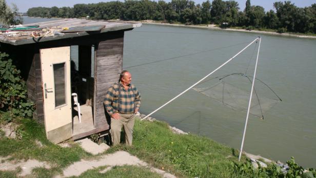 Ein Mann steht neben einer kleinen Holzhütte mit einem Fischernetz am Flussufer.