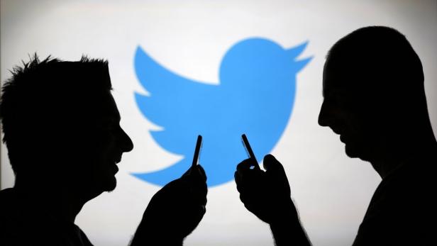 Zwei Silhouetten von Personen, die Smartphones vor dem Twitter-Logo halten.