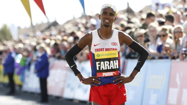 Mo Farah steht mit den Händen auf den Hüften vor einer Menschenmenge.