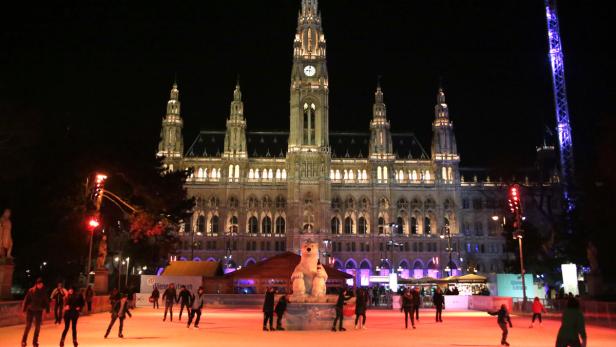 Menschen laufen auf einer Eisbahn vor dem Wiener Rathaus bei Nacht.