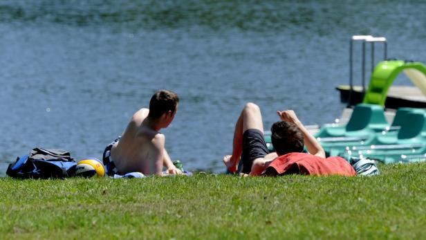 Zwei Männer liegen am Ufer eines Sees in der Sonne.