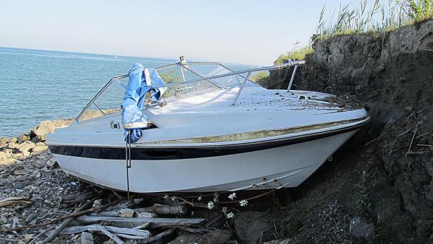 Ein gestrandetes, weißes Motorboot liegt an einem steinigen Ufer.