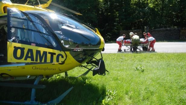 Ein gelber ÖAMTC-Rettungshubschrauber steht neben einem Team, das eine Person auf einer Trage transportiert.