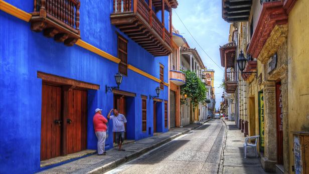Zwei Männer unterhalten sich auf einer Straße mit farbenfrohen Kolonialgebäuden.