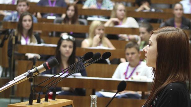 Eine junge Frau spricht vor einem Publikum in einem Hörsaal in ein Mikrofon.
