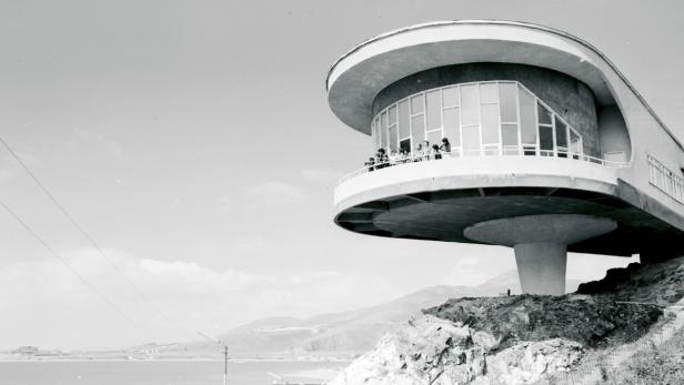 Ein futuristisches Gebäude auf einem Hügel mit Blick auf das Meer, in Schwarzweiß.
