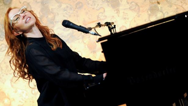 Eine Frau mit Brille spielt Klavier und singt in ein Mikrofon.