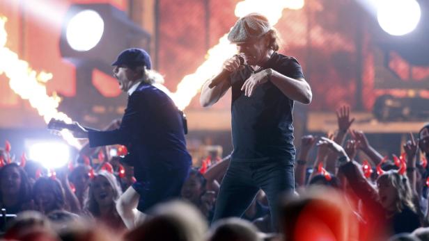AC/DC tritt vor jubelnden Fans mit roten Teufelshörnern auf einer Bühne mit Flammeneffekten auf.