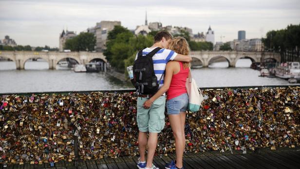 Ein Paar umarmt sich auf einer Brücke in Paris, deren Geländer mit Liebesschlössern behangen ist.